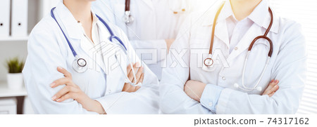 Unknown woman-doctor standing straight with arms crossed in clinic, close-up. Medical team ready to stop coronavirus pandemic. Medicine concept 74317162