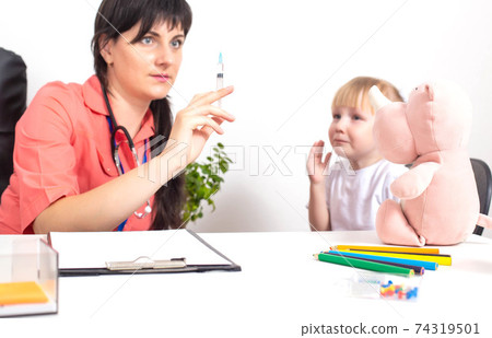 The doctor holds a medical syringe in his hands and a little girl cries nearby in fright. The concept of fear of vaccinations and injections in children, copy space The doctor holds a medical syringe in his hands and a little girl cries nearby in fright. The concept of fear of vaccinations and injections in children, copy space 74319501