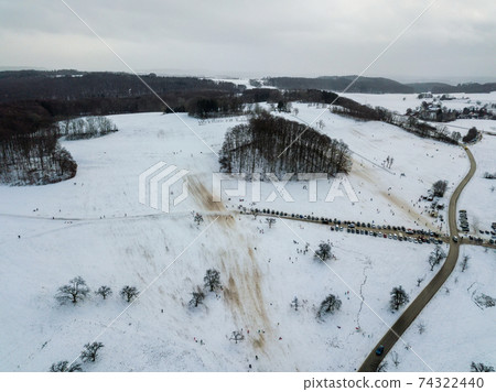 Aerial view of people enjoying a winter day by sledding on a small ski slope during winter holidays in a small village on the Swabian Alps in Southern Germny. The ski lift is not operating due to the 74322440