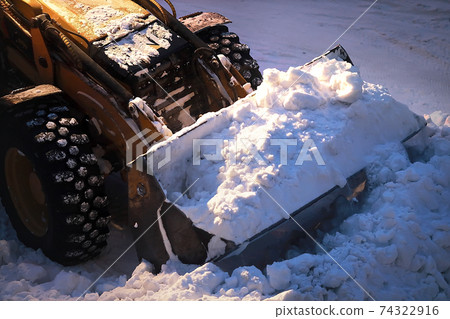 Excavator with a full bucket of snow. Snow removal from city streets at night.  74322916