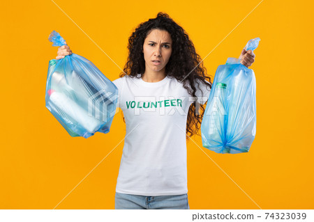 Displeased Female Volunteer Holding Plastic Garbage Bags On Yellow Background 74323039