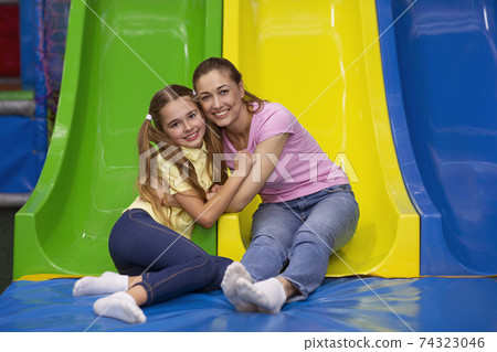 Portrait of happy mother and her teen daughter hugging near colorful slide at indoor entertainment centre for kids 74323046
