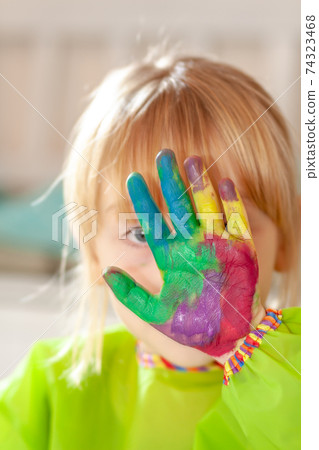 Little girl hiding behing her watercolour painted hand at home during the pandemic lockdown Little girl hiding behing her watercolour painted hand at home during the pandemic lockdown 74323468