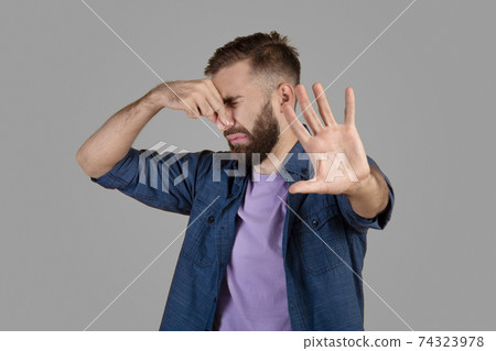 Terrible smell. Millennial hipster guy closing his nose and gesturing STOP, feeling disgusted on grey studio background Terrible smell. Millennial hipster guy closing his nose and gesturing STOP, feeling disgusted on grey studio background 74323978