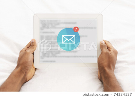 African Man Reading Email Messages On Tablet Lying In Bedroom 74324157