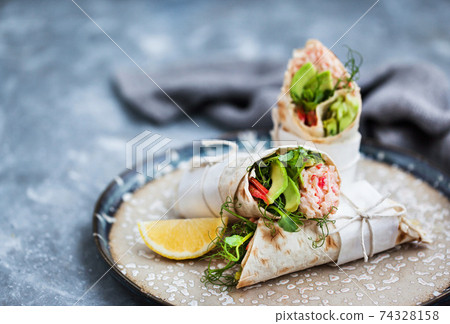 Fresh and healthy wrapped tortilla with crab salad, cucumber, avocado, pepper and green herbs 74328158
