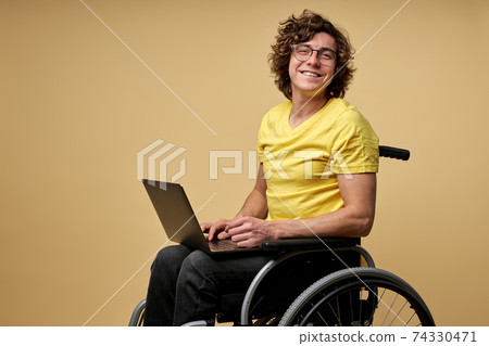 disabled caucasian man sits in a wheelchair with laptop 74330471