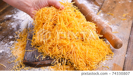 Italian egg pasta, homemade and fresh on a wooden table. Tagliatelle pasta is thin. In hand Italian egg pasta, homemade and fresh on a wooden table. Tagliatelle pasta is thin. In hand 74330807