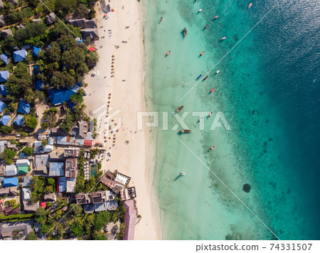 Aerial view of pool, umbrellas, sandy beach with green Palm trees. Coast of Indian ocean at sunset in summer. Zanzibar, Africa. Top view. Landscape with azure water, parasols, palm trees. Luxury Aerial view of pool, umbrellas, sandy beach with green Palm trees. Coast of Indian ocean at sunset in summer. Zanzibar, Africa. Top view. Landscape with azure water, parasols, palm trees. Luxury 74331507