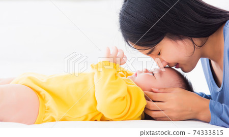 mother kissing her infant newborn baby in a white bed 74333815