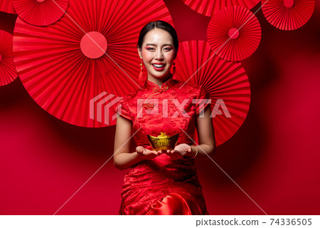 Beautiful smiling Asian woman holding ancient Chinese gold ingot 74336505