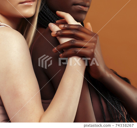 two pretty girls african and caucasian blond posing cheerful together on brown background, ethnicity diverse lifestyle people concept two pretty girls african and caucasian blond posing cheerful together on brown background, ethnicity diverse lifestyle people concept 74338267