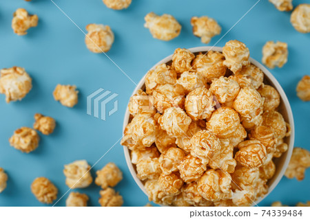 Caramel of the popcon in a white cup with a scissor on a blue background. 74339484
