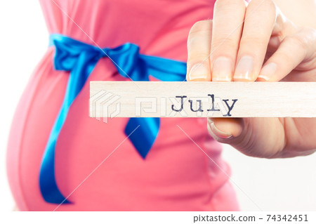 Pregnant woman in pink dress with blue ribbon showing word july Pregnant woman in pink dress with blue ribbon showing word july 74342451