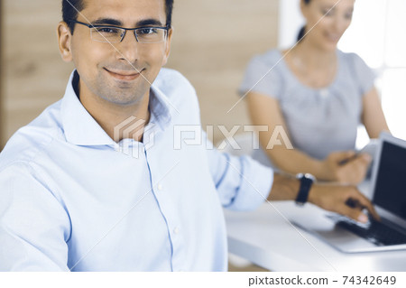 Businessman and business woman discussing questions while using a computer in modern office. Portrait of male entrepreneur at meeting. Group of diverse people 74342649