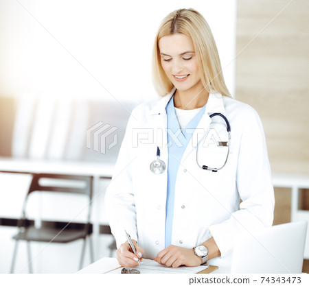 Doctor woman controls medication history records and exam results while using clipboard in sunny hospital . Medicine and healthcare concept Doctor woman controls medication history records and exam results while using clipboard in sunny hospital . Medicine and healthcare concept 74343473
