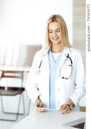 Woman-doctor controls medication history records and exam results while using tablet computer in sunny hospital. Medicine and healthcare concept Woman-doctor controls medication history records and exam results while using tablet computer in sunny hospital. Medicine and healthcare concept 74343475