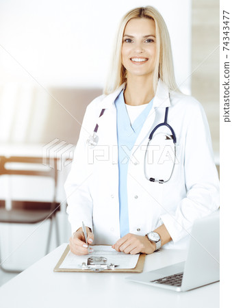 Doctor woman controls medication history records and exam results while using clipboard in sunny hospital . Medicine and healthcare concept 74343477