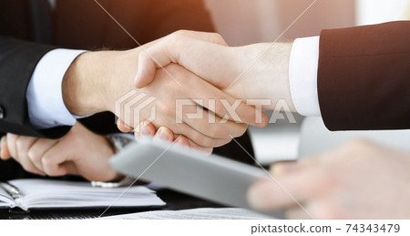 Businessman shaking hands with his colleague above the glass desk in sunny modern office, close-up. Unknown business people at meeting Businessman shaking hands with his colleague above the glass desk in sunny modern office, close-up. Unknown business people at meeting 74343479