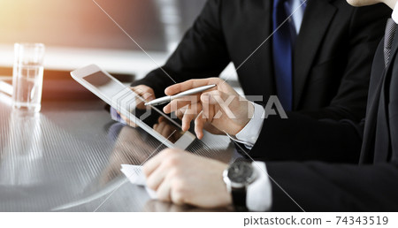 Businessman using tablet computer and work together with his colleague in sunny modern office, close-up. Unknown business people at meeting. Teamwork and partnership concept 74343519