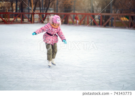 Girl uncertainly stands on figure skates on an ice rink and tries to ride Girl uncertainly stands on figure skates on an ice rink and tries to ride 74343773