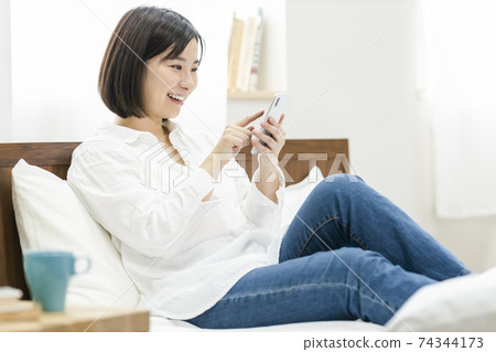 Young woman operating a smartphone on the bed Young woman operating a smartphone on the bed 74344173