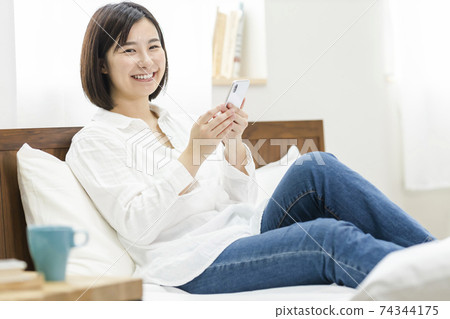 Young woman operating a smartphone on the bed Young woman operating a smartphone on the bed 74344175