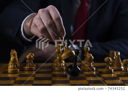 concept of strategy and business planning, businessman behind a chessboard white queen beats a black chess piece, strategy and tactics, readiness for battle, start of battle 74345252