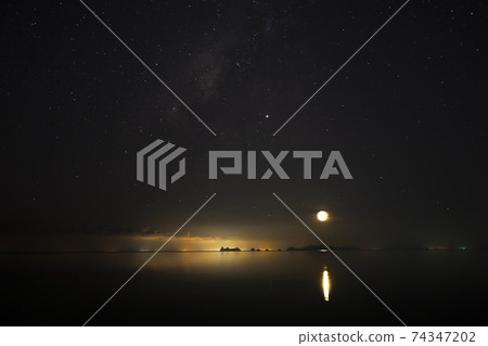 The sky with star and moon is above on light of city and mountain at the lake in dark night. 74347202