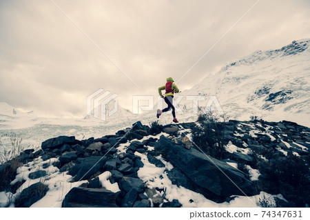 Woman trail runner cross country running up to winter snow mountain top 74347631