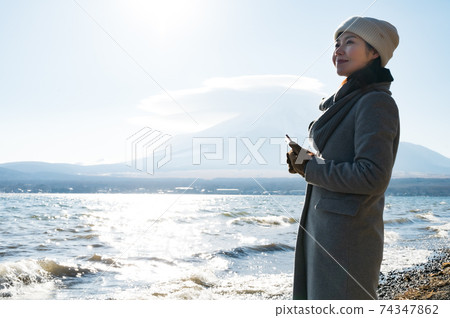 A woman taking a picture of the shores of Lake Yamanaka in winter with a smartphone camera A woman taking a picture of the shores of Lake Yamanaka in winter with a smartphone camera 74347862