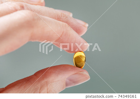 Female hand holding a small yellow capsule of nutritional supplement. Food supplement, vitamin D, omega, vitamin C. Female hand holding a small yellow capsule of nutritional supplement. Food supplement, vitamin D, omega, vitamin C. 74349161