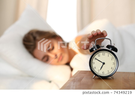 Sleepy young woman stretching hand to ringing alarm willing turn it off. Early wake up, not getting enough sleep, getting work concept. 74349219