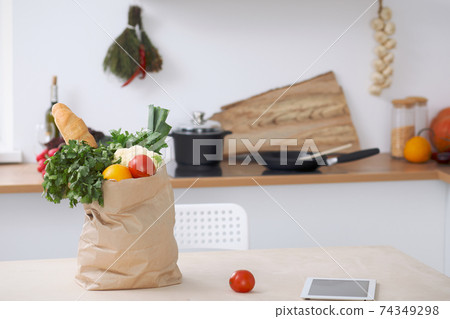 Paper bag full of vegetables on the table in kitchen interiors. Healthy meal and vegetarian concept Paper bag full of vegetables on the table in kitchen interiors. Healthy meal and vegetarian concept 74349298