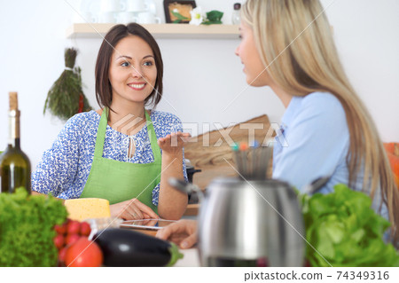 Two young happy woman making cooking in the kitchen. Friendship and culinary concept Two young happy woman making cooking in the kitchen. Friendship and culinary concept 74349316