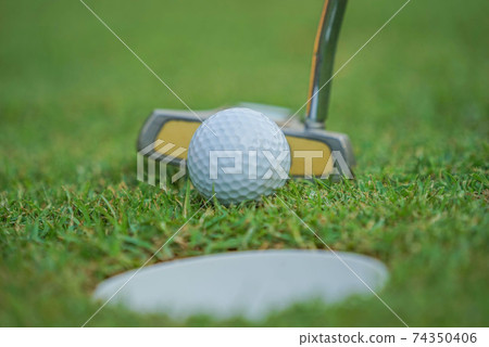 Golf clubs and golf balls on a green lawn in a beautiful golf course with morning sunshine. The ball at the hole on the golf course. 74350406