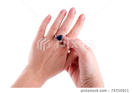 Woman trying on a heart shaped blue sapphire precious ring isolated on white background. Close up of diamond ring on female hand. White golden ring with blue gemstone. Jewelry, fashion jewellery theme 74350921