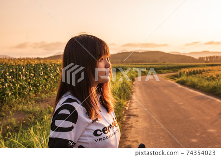 Female road racer looking at the sky dyed in the sunset 74354023