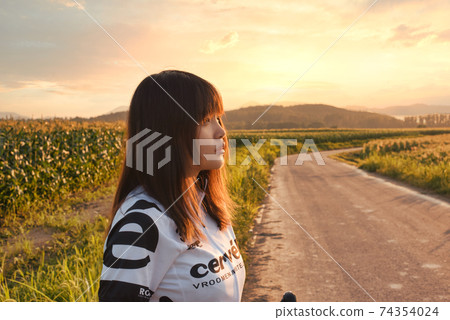 Female road racer looking at the sky dyed in the sunset 74354024