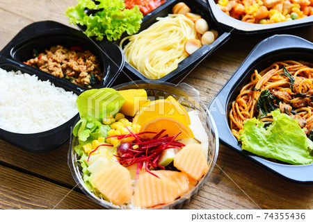 Service food order online delivery Spaghetti italian pasta macaroni cheese with sausage rice and fruit on food box, Food delivery in take away boxes package on wooden table at home. 74355436