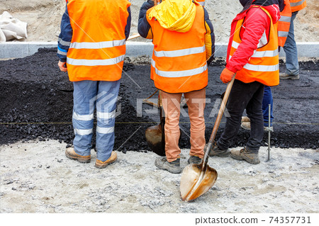 A team of road construction workers in orange overalls hold a meeting at a work site. A team of road construction workers in orange overalls hold a meeting at a work site. 74357731