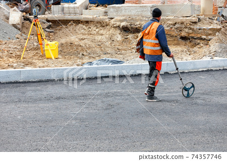 A road worker measures the jobsite with an electronic measuring wheel. A road worker measures the jobsite with an electronic measuring wheel. 74357746