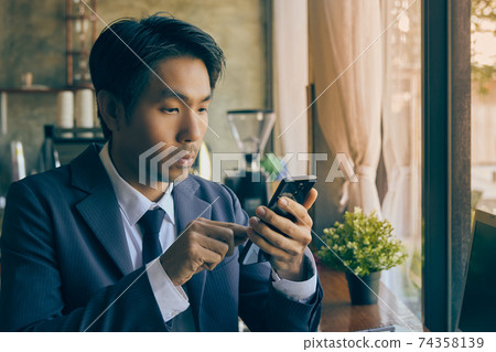 Zoom View Front Right Asian Businessman Touch Smartphone in Coffee Shop Scene in Vintage Tone Zoom View Front Right Asian Businessman Touch Smartphone in Coffee Shop Scene in Vintage Tone 74358139