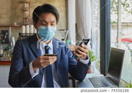 Zoom View Front Sitting Asian Businessman Wear Face Mask Online Shopping by Smartphone Zoom View Front Sitting Asian Businessman Wear Face Mask Online Shopping by Smartphone 74358186