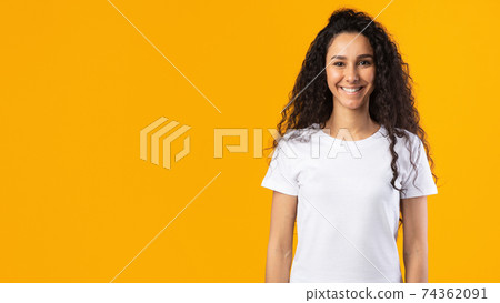 Cheerful Brunette Lady Wearing White T-Shirt Standing Over Yellow Background Cheerful Brunette Lady Wearing White T-Shirt Standing Over Yellow Background 74362091
