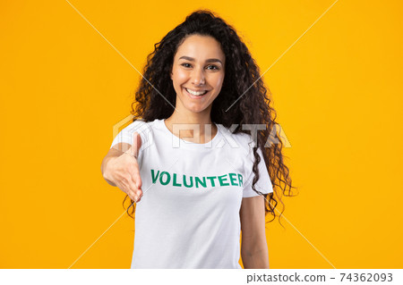 Cheerful Volunteer Woman Offering Hand For Handshake Over Yellow Background Cheerful Volunteer Woman Offering Hand For Handshake Over Yellow Background 74362093