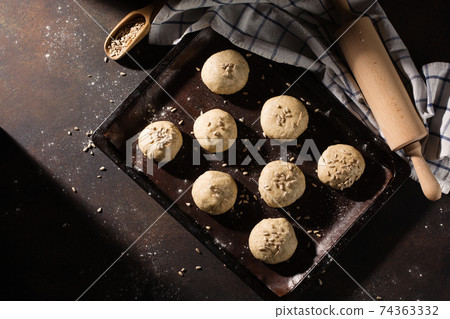 Homemade wholemeal buns dough on wooden table with flour, rolling-pin on dark rustic background. Homemade wholemeal buns dough on wooden table with flour, rolling-pin on dark rustic background. 74363332