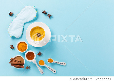 Turmeric golden milk latte with spices, cinnamon, honey and Sleep mask on blue background. 74363335
