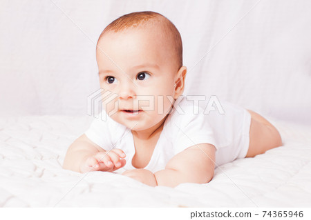 Adorable baby lying on the stomach at the white Adorable baby lying on the stomach at the white 74365946