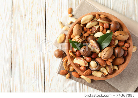 Bowl with different tasty nuts on white wooden background Bowl with different tasty nuts on white wooden background 74367095